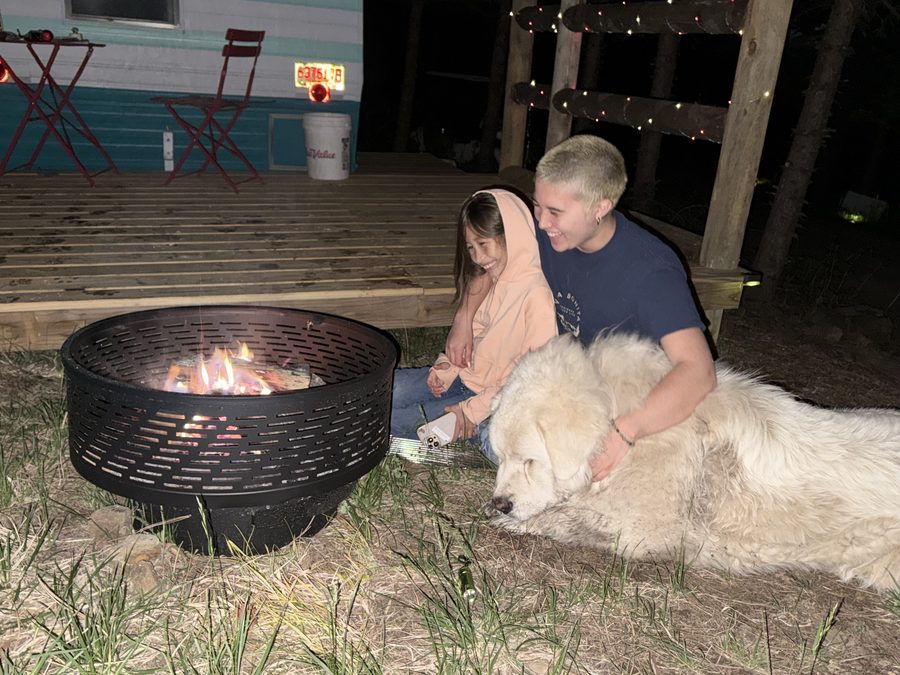 A child and young adult by a fire pit with a Great Pyrenees dog on a cool summer night