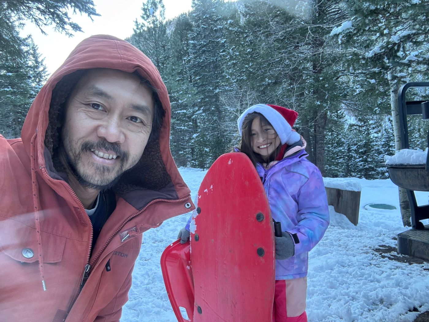 Duc and a smiling child holding a red sled on a snowy morning on the property